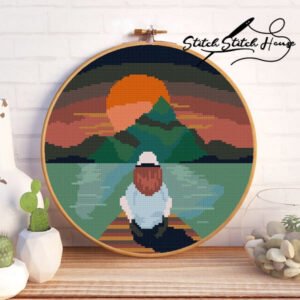 Modern cross stitch pattern of a girl sitting on a wooden dock watching the sunset over mountains and a lake