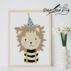 Handmade cross stitch pattern of a smiling brown lion wearing a blue polka dot party hat and black striped shirt