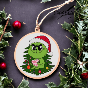 Cute Grinch wearing Santa hat sitting on a Christmas tree holding a pink heart cross stitch pattern design